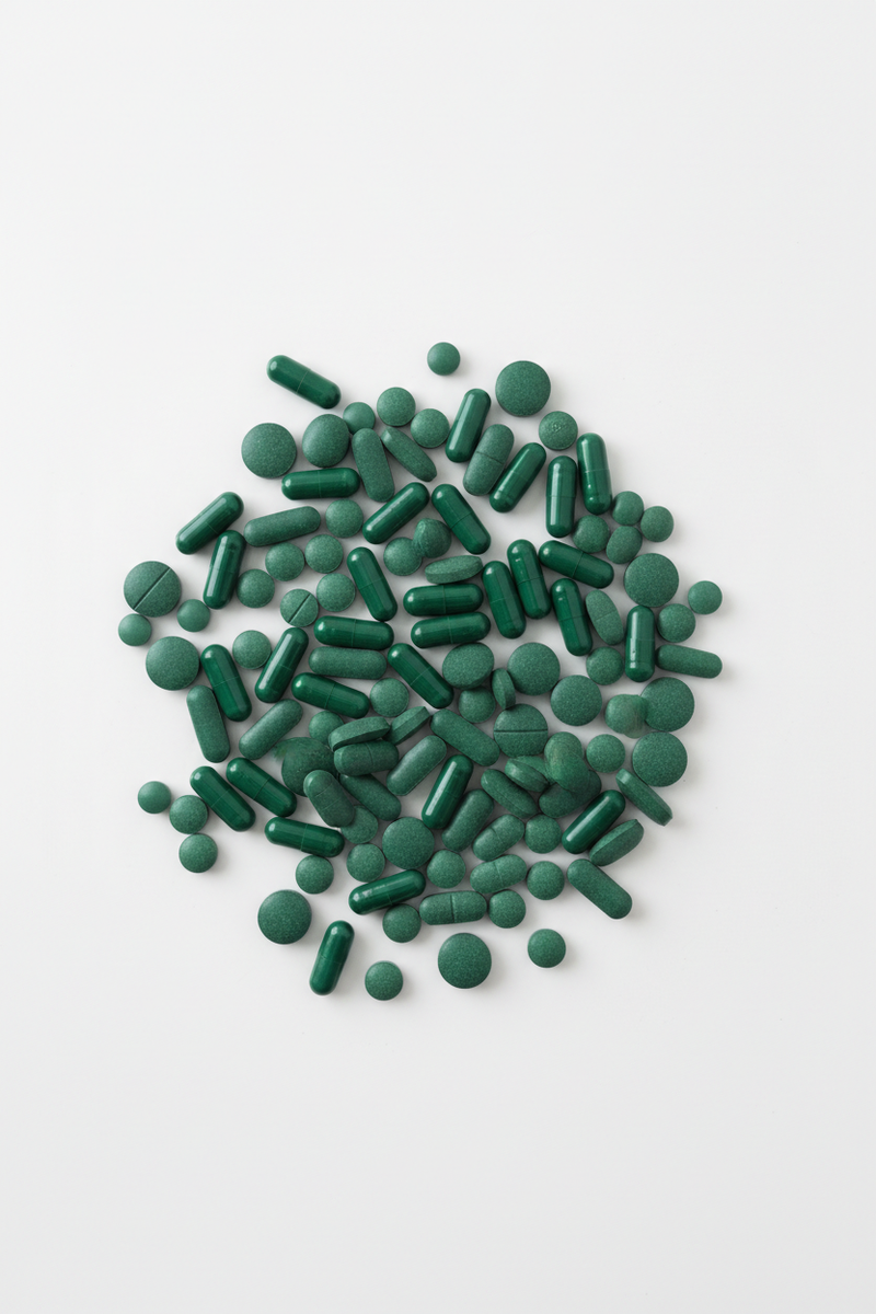 Make a vertical image of many pills lying on a. white floor. Make these pills forest green